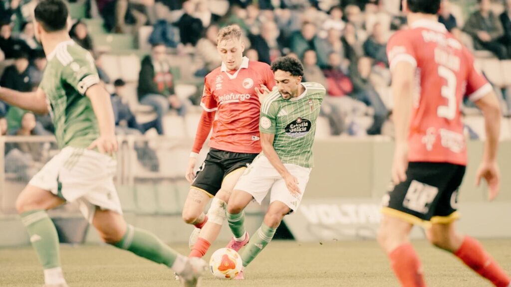 nionistas vs Racing de Ferrol en A Malata: jugadores blanquinegros luchando en un campo embarrado durante un partido de Primera RFEF.